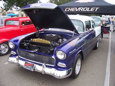2002 Ford Mustang - A customized 1955 Chevrolet Bel Air is displayed with its hood open, parked next to a red hot rod under a Chevrolet tent.