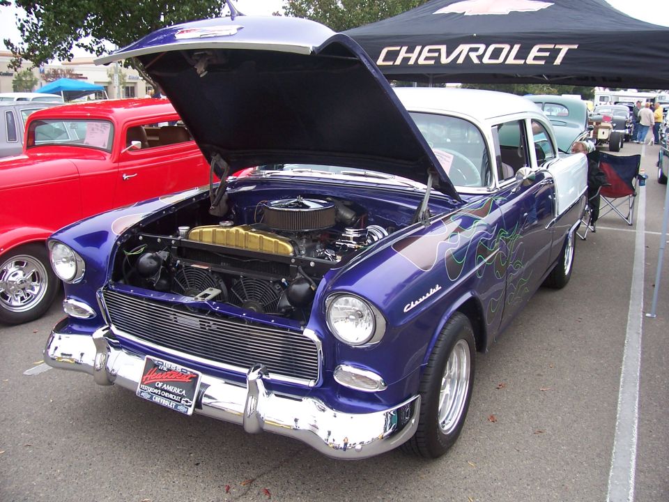 Purple 1955 Chevy Bel Air with flames and open hood, red hot rod next to it, Chevrolet tent in background