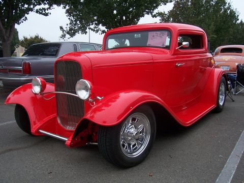 2002 Ford Mustang - A bright red hot rod coupe is parked next to other vehicles under a cloudy sky.