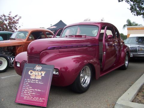 2002 Ford Mustang - A custom maroon coupe is displayed with a sign detailing its features, parked next to other vehicles.