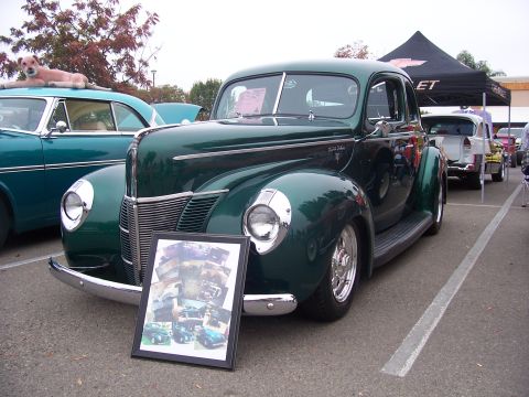 2002 Ford Mustang - A vintage green coupe is displayed with a collage of photographs in front of it at an outdoor event.