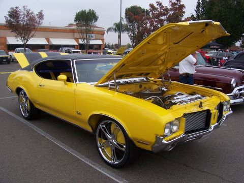 2002 Ford Mustang - A bright yellow classic car is parked with its hood open, revealing the engine bay. The car has a black roof and racing stripes.