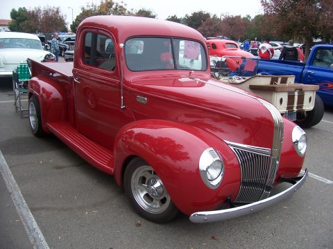 2002 Ford Mustang - A classic red pickup truck is displayed at an outdoor event with other vehicles visible.