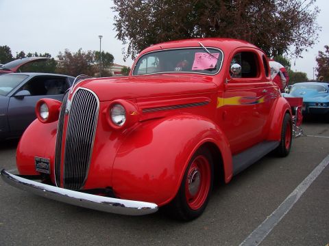 2002 Ford Mustang - A bright red vintage coupe is parked at an outdoor event, with other vehicles visible in the background.
