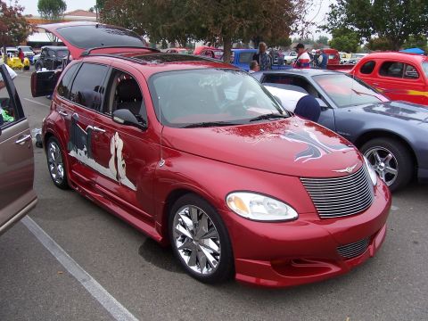 2002 Ford Mustang - Customized red Chrysler PT Cruiser with graphics and aftermarket wheels at an outdoor car show.