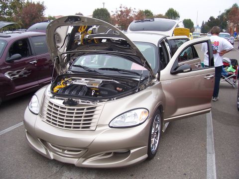 2002 Ford Mustang - A customized Chrysler PT Cruiser is displayed with its hood and door open, parked next to another PT Cruiser.