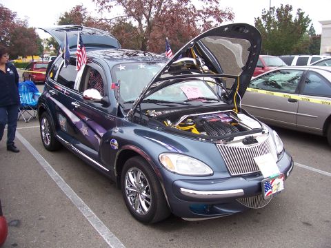 2002 Ford Mustang - A customized Chrysler PT Cruiser is displayed with its hood and trunk open, decorated with patriotic American-themed graphics and flags.