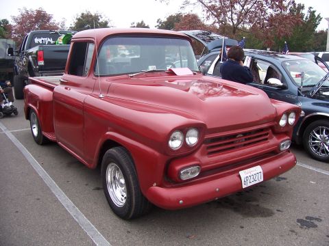 2002 Ford Mustang - A classic red pickup truck is displayed at an outdoor event, with other cars visible in the background.