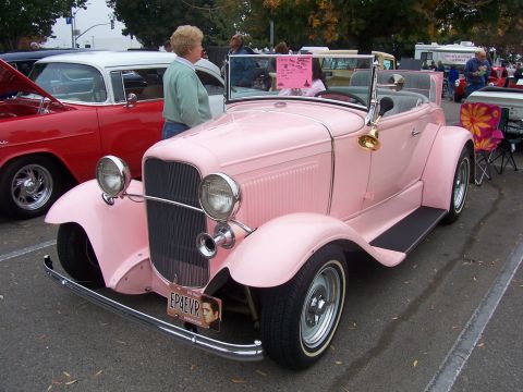 2002 Ford Mustang - A pink convertible hot rod is parked next to a red car at an outdoor event.