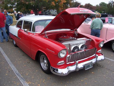 2002 Ford Mustang - A classic red and white 1955 Chevrolet Bel Air is displayed with its hood open, revealing the engine and a prominent chrome radiator.
