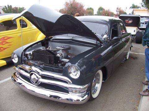 2002 Ford Mustang - Customized 1950 Ford sedan on display with its hood open, next to a yellow hot rod.