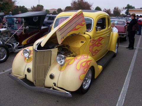 2002 Ford Mustang - A custom hot rod with flame paint and its hood open is displayed at an outdoor event.