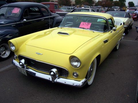 2002 Ford Mustang - A bright yellow 1955 Ford Thunderbird is parked in a lot, with other vehicles visible in the background.