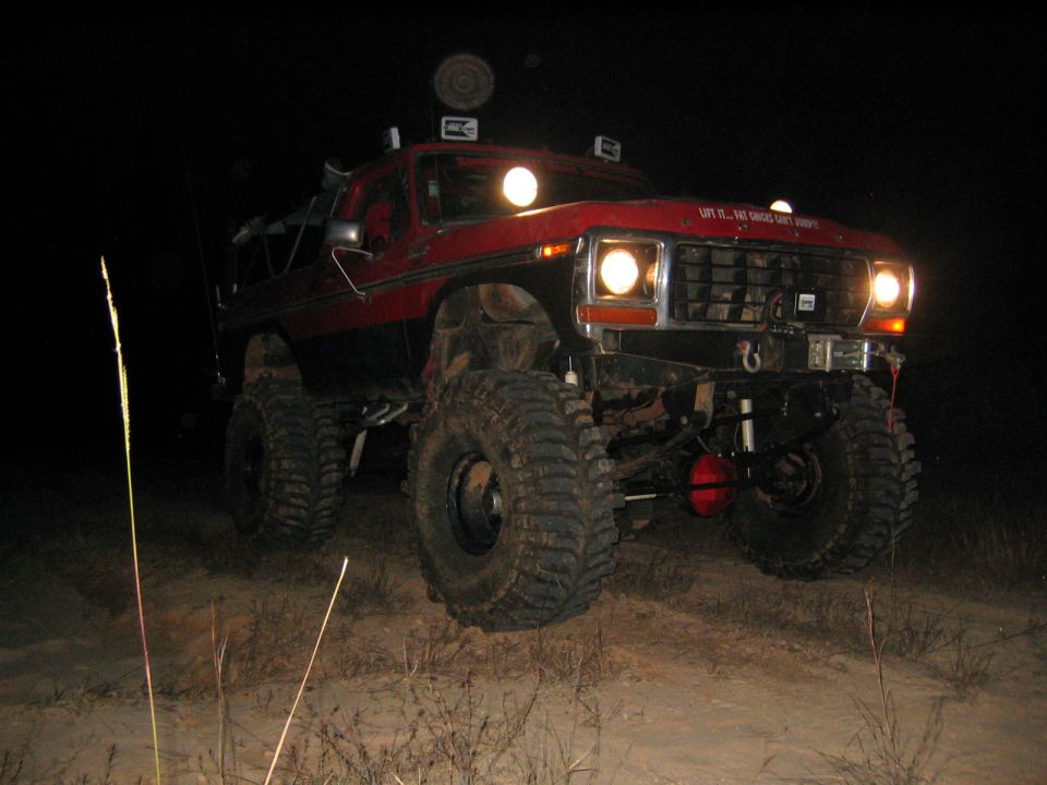 red lifted SUV with big tires, driving at night. Text on hood says 'Lift it... Fat chicks can't jump'