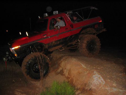 1979 Ford Bronco - This red SUV is tackling a challenging muddy incline in the dark, with its large tires digging into the dirt.