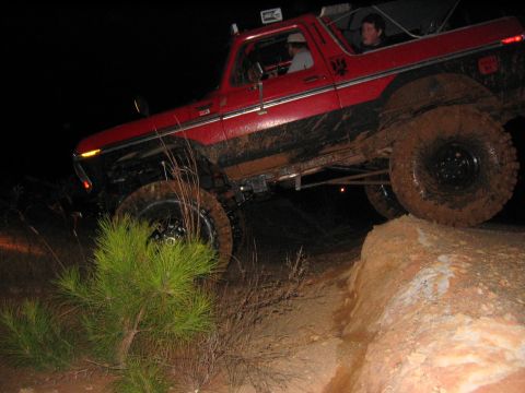 1979 Ford Bronco - A red SUV navigates a muddy, off-road trail in the dark.