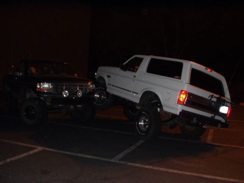 1993 Ford Bronco - Two lifted Ford Broncos are parked at night, one with its front end visible and the other with its rear end.