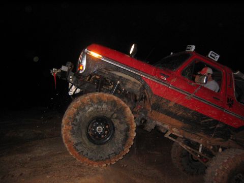 1979 Ford Bronco - Muddy red SUV navigates terrain in the dark, driver behind the wheel.