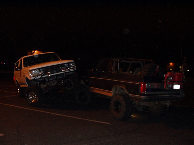 Lifted white Bronco and dark lifted pickup with big tires in a dark parking lot at night