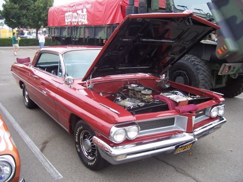 2002 Ford Mustang - A classic red 1959 Pontiac Bonneville is displayed with its hood open, parked near a large military vehicle.