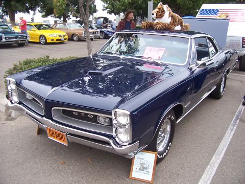 2002 Ford Mustang - A 1966 Pontiac GTO is displayed at an outdoor event, with other vehicles and people visible.