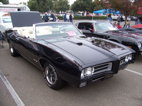 2002 Ford Mustang - A classic black Pontiac GTO convertible is displayed at an outdoor event, parked next to another vehicle.
