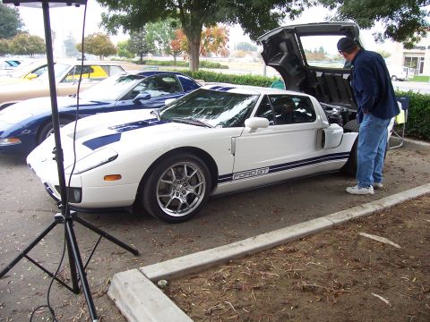 2002 Ford Mustang - A white Ford GT with blue racing stripes is displayed with its engine compartment open, alongside other vehicles.