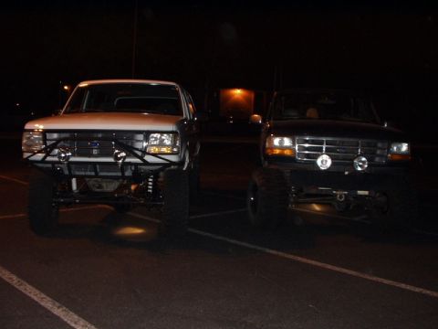 1993 Ford Bronco - Two modified Ford trucks, likely from the early 1990s, are parked side-by-side at night.