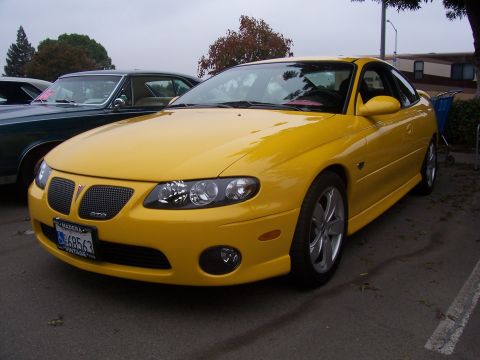 2002 Ford Mustang - A yellow Pontiac GTO is parked next to another car, with trees and buildings in the background.