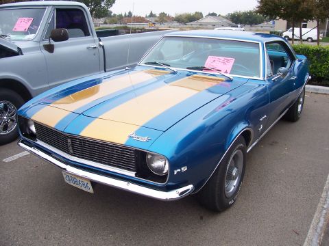 2002 Ford Mustang - A blue 1967 Chevrolet Camaro RS with gold racing stripes is parked next to a pickup truck.