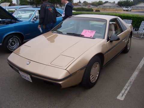 2002 Ford Mustang - A gold Pontiac Fiero is parked next to a blue car at an outdoor event.