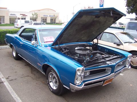 2002 Ford Mustang - A blue 1966 Pontiac GTO is parked with its hood open, revealing the engine compartment. Another vehicle is visible to the right.