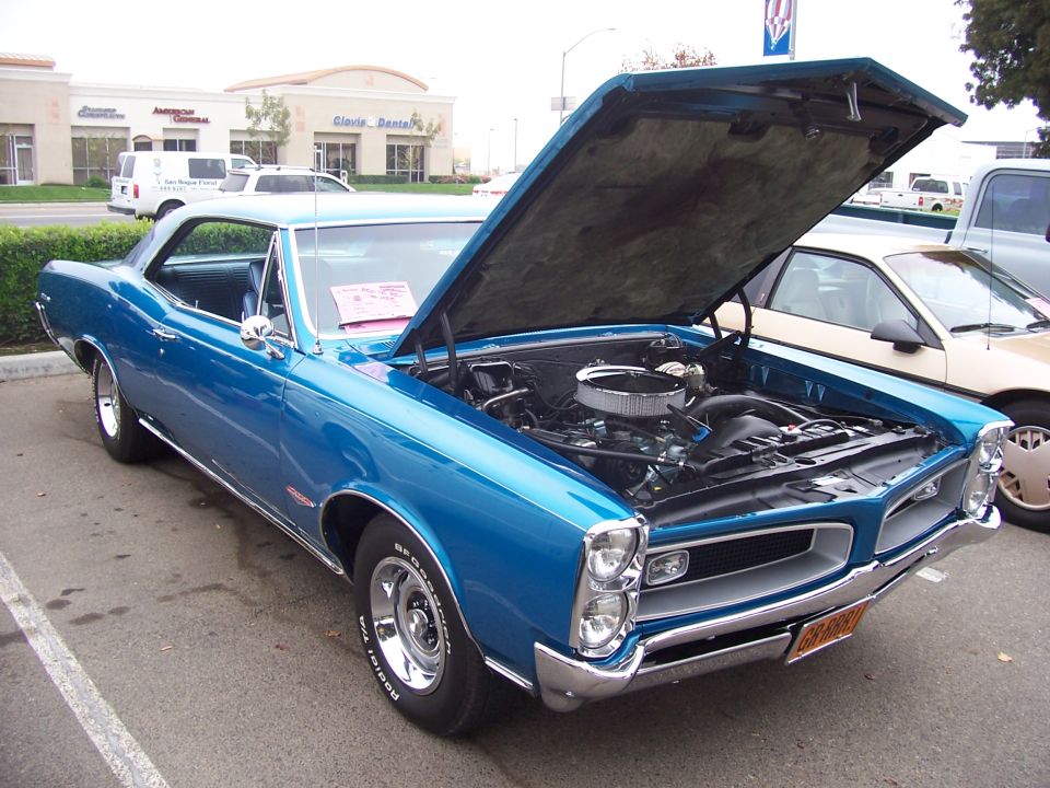 Blue 1966 Pontiac GTO with hood open, showing the engine. Another car is parked next to it