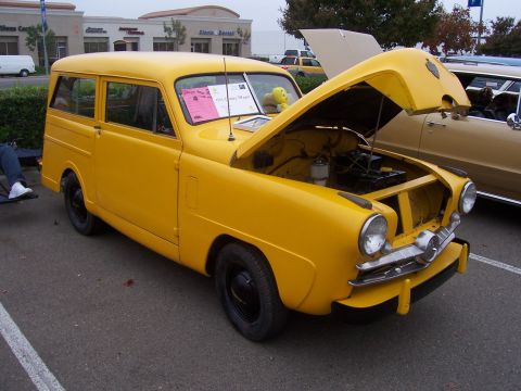 2002 Ford Mustang - A yellow station wagon is parked with its hood open, displaying a pink sign on the windshield.
