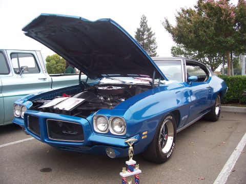 2002 Ford Mustang - A blue 1970 Pontiac GTO is displayed with its hood open, next to another vehicle, with a trophy in the foreground.