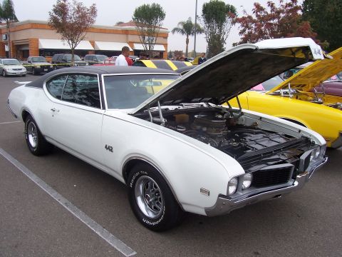 2002 Ford Mustang - A white 1969 Oldsmobile 442 is displayed with its hood open, parked alongside other vehicles.