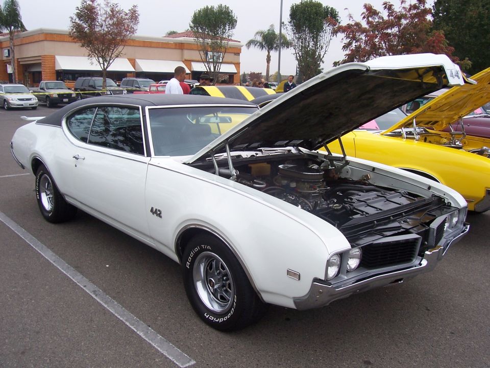 White 1969 Oldsmobile 442 with hood open, parked next to a yellow car