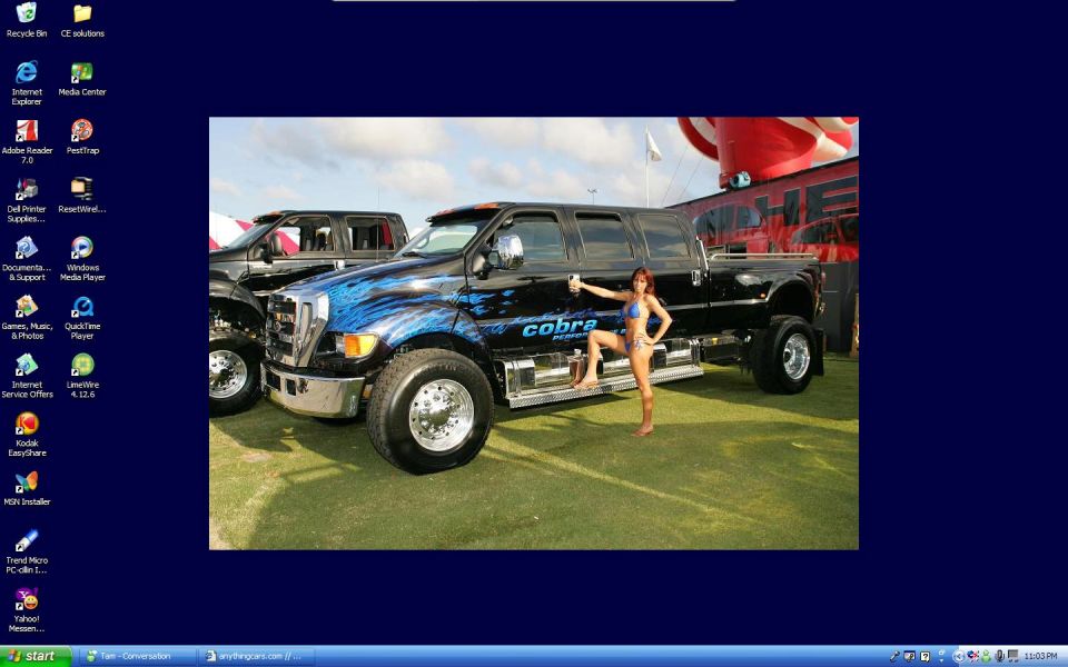 Black custom Ford F-650 pickup truck with blue flame graphics and 'cobra' text, parked next to another truck, with a woman in a bikini posing