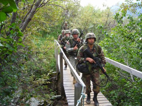 2003 Jeep TJ - A group of soldiers traverses a narrow wooden bridge amidst dense foliage.