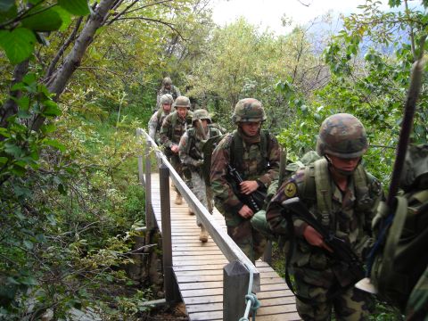 2003 Jeep TJ - A group of soldiers in camouflage uniforms traverses a wooden bridge through a wooded area.