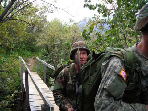 2003 Jeep TJ - Two soldiers traverse a narrow wooden bridge surrounded by dense foliage.