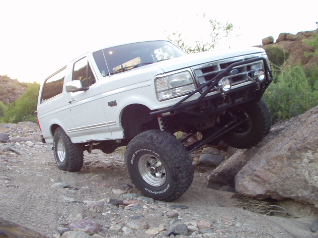 White lifted Ford Bronco flexing suspension while crawling over rocks off-road