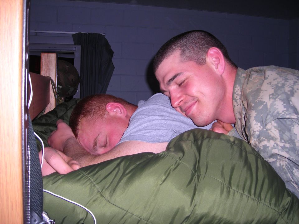Two soldiers sleeping in bunk beds, one with head on the other's shoulder