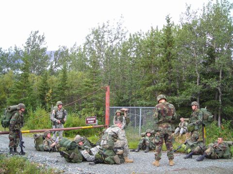 2003 Jeep TJ - A group of soldiers in camouflage uniforms with large backpacks are gathered near a gate and fence in a wooded area.
