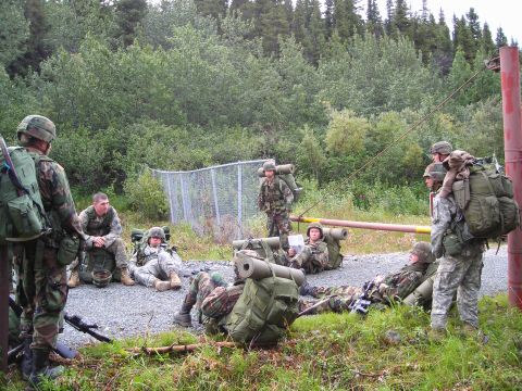 2003 Jeep TJ - A group of soldiers in camouflage uniforms are taking a break outdoors, with large backpacks and gear around them.