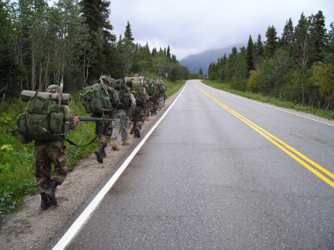 2003 Jeep TJ - A column of soldiers marches along a highway through a wooded, mountainous area under an overcast sky.