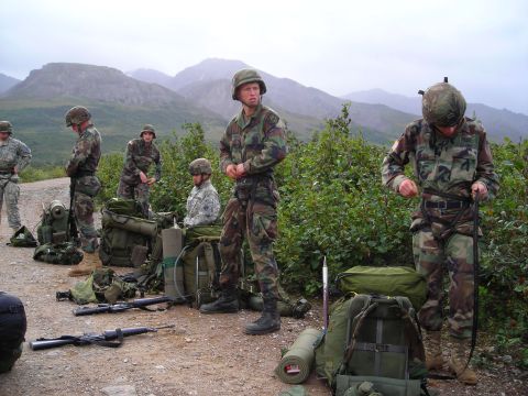 2003 Jeep TJ - A group of soldiers prepares their gear outdoors with backpacks and rifles laid out on the ground.