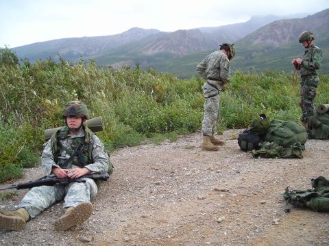 2003 Jeep TJ - Soldiers in uniform with gear resting outdoors with mountains in the background.