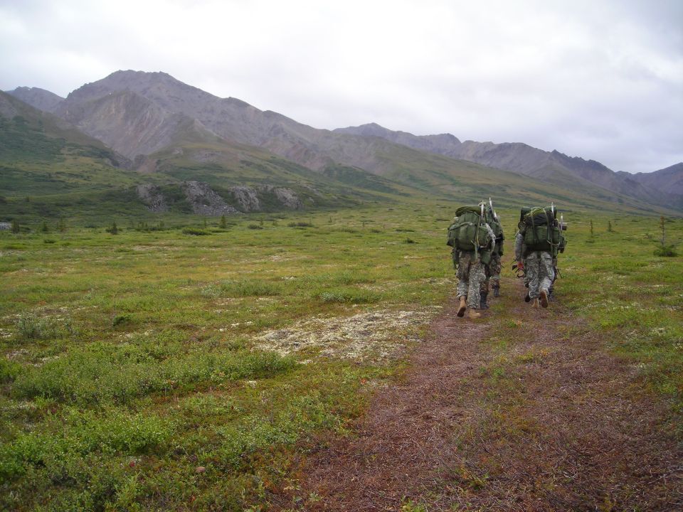 Soldiers hiking through a grassy plain towards mountains