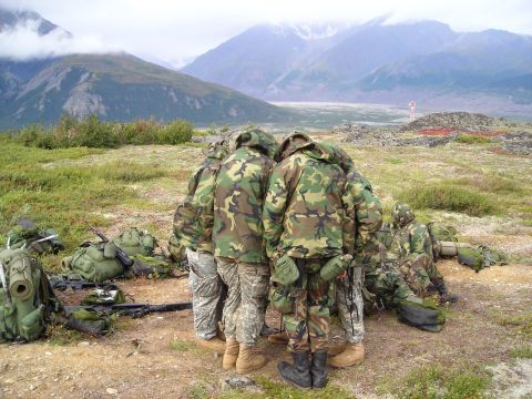 2003 Jeep TJ - A group of soldiers in camouflage uniforms huddle together in a remote, mountainous area, surrounded by their gear.